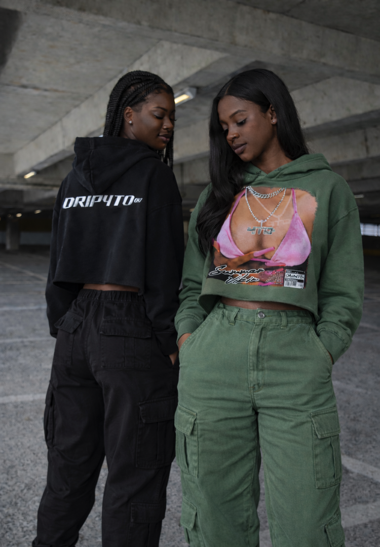 Two women standing in an urban setting, one wearing a black hoodie with 'DRIP4TO' text and the other in a green hoodie with a graphic design.