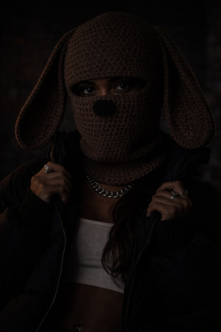 Person wearing a dark, textured hood with long ears in a dimly lit setting