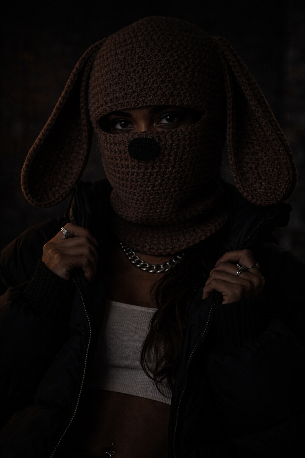 Person wearing a dark, textured hood with long ears in a dimly lit setting